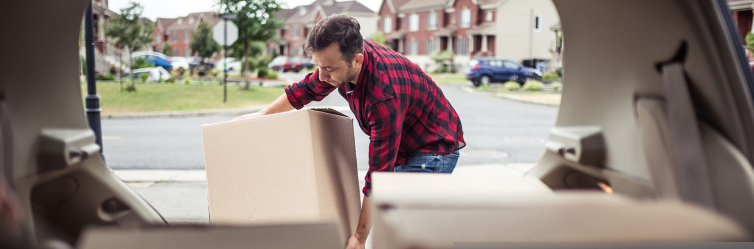 man unpacking boxes from the back of ac car in a neighborhood