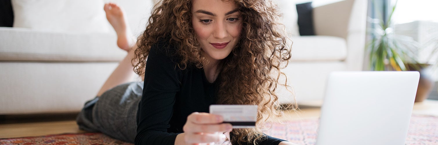 Adolescente en línea de compras en el piso de la sala mientras sostiene la tarjeta de crédito
