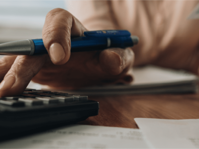 Hand holding pen and using calculator.