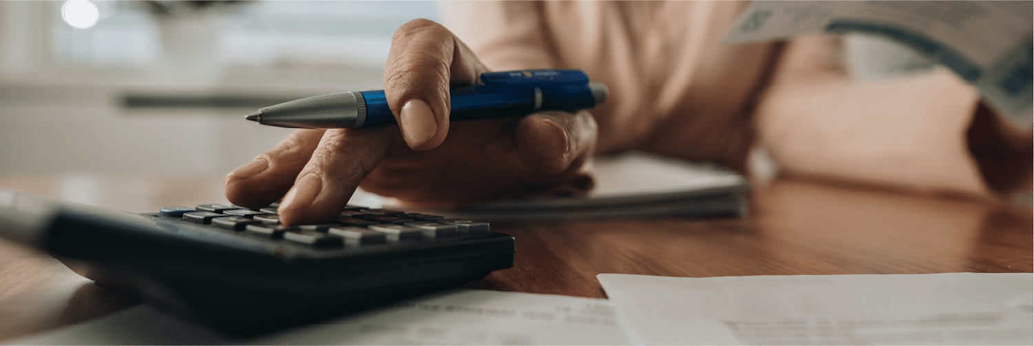 Hand holding pen and using calculator.