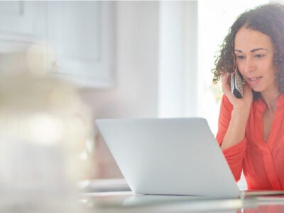 Woman on the phone looking at a laptop.