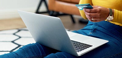 Woman sitting by the sofa shopping online on laptop with bank card in hand.