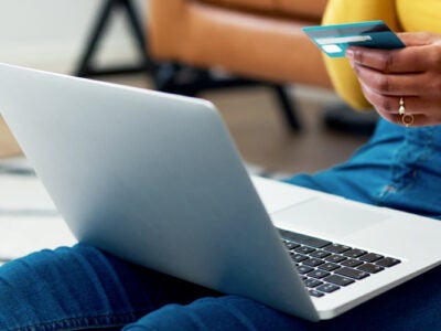 Woman sitting by the sofa shopping online on laptop with bank card in hand.