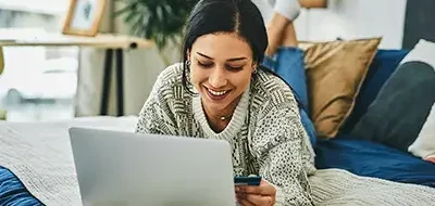 A woman in bed shopping online with a credit card.