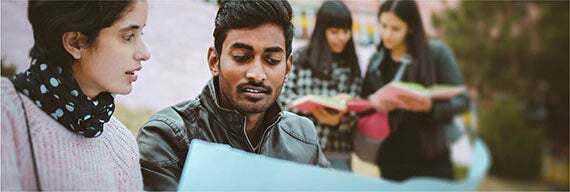 A young man and young woman sitting down looking at a college textbook.